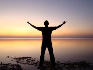 Silhouette of man with arms outstretched in worship as the sun rises